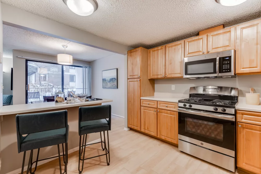 Modern kitchen with light wood cabinets, stainless steel appliances, breakfast bar, and two dark stools.
