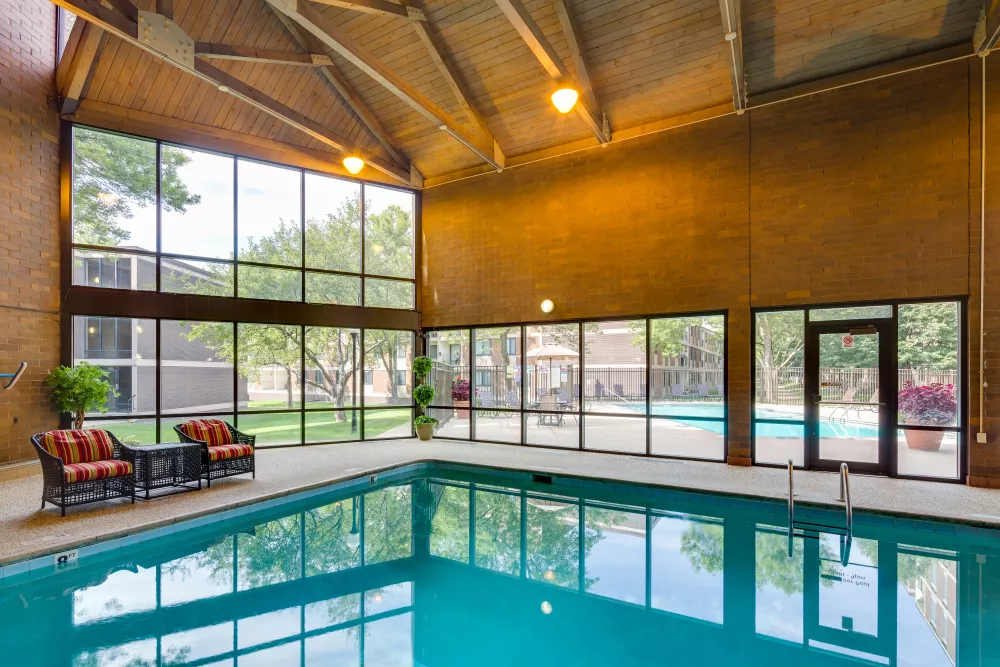 Spacious indoor swimming pool room with vaulted ceilings and large windows revealing an outdoor pool and landscaped grounds.