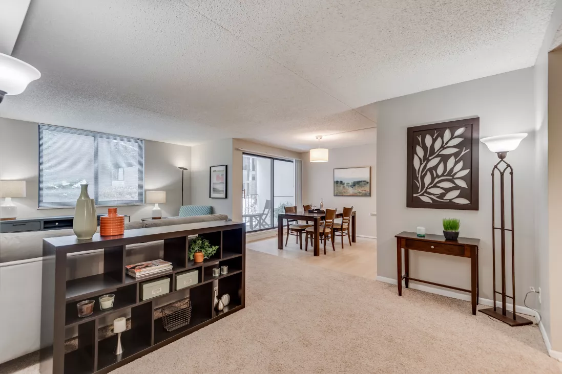 Open concept living and dining room with neutral decor, dark wood shelving unit, and balcony access.